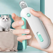 Hand holding white and mint green pet nail clipper with fluffy cat sitting on couch in background