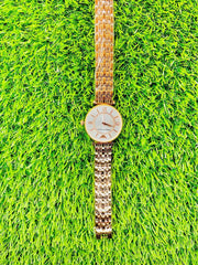 Elegant gold Emporio Armani women's watch with linked metal band on vibrant green grass