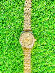 Luxury gold women's wristwatch with stone-studded bezel and linked bracelet on green grass