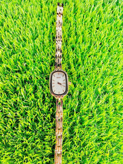 Slim oval women's wristwatch with dual-tone metal band and minimalist white dial on green grass