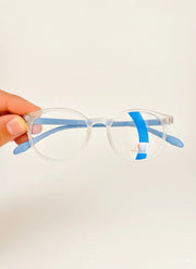 Hand holding clear round eyeglasses with blue temple arms against plain background