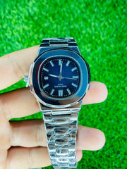 Silver metal wristwatch with blue dial, date display, and luminous markers held against green grass background