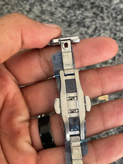 Close-up of a hand holding a silver metal watch clasp with a blue dial visible beneath plastic wrapping