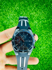 Close-up of hand holding a black Westchi hi mens chronograph sports watch with black and white striped rubber strap on green grass background